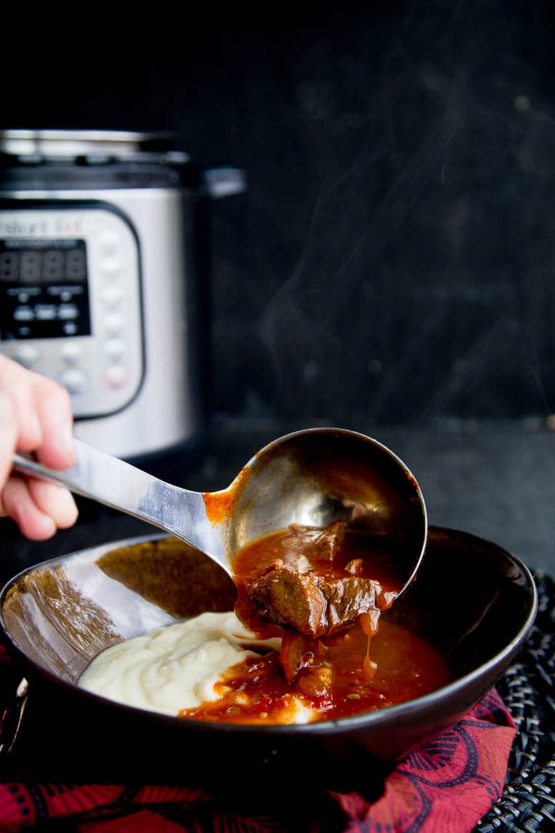 Goulash ladled into a bowl with cauliflower mash with an Instant Pot sitting in the background.