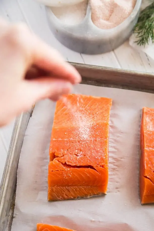 A salmon fillet on a parchment lined sheet pan being salted.
