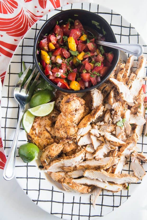 Chipotle-Lime Grilled Chicken with Strawberry Mango Salsa on a platter with fresh limes and cilantro.