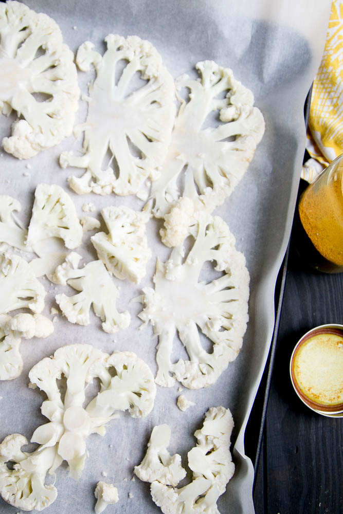 Prepping roasted cauliflower with curry powder on a parchment-lined baking sheet. 