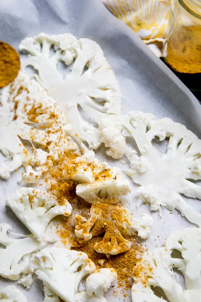 Prepping roasted cauliflower with curry powder on a parchment lined baking sheet.