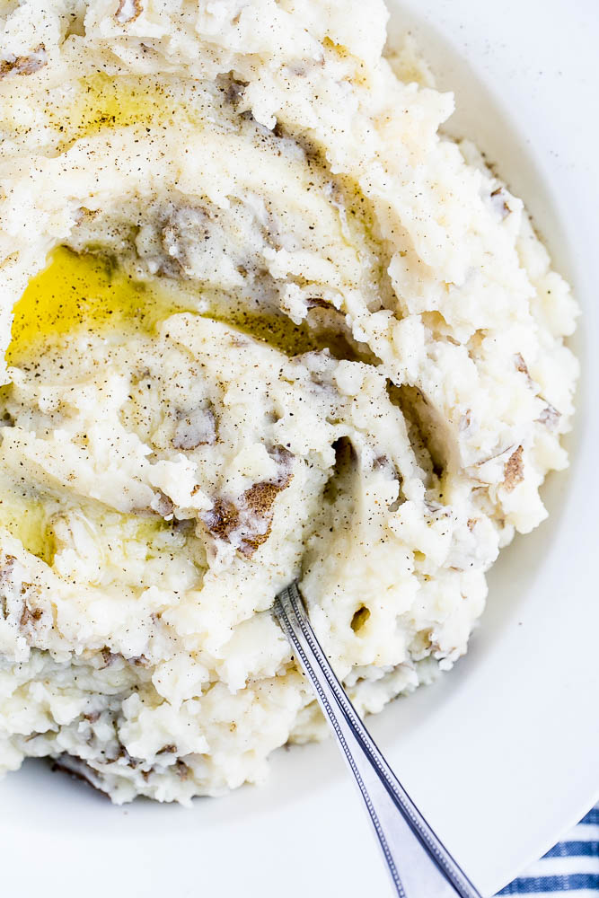 Finished mashed potatoes in a large serving bowl with a little melted butter drizzled on top.