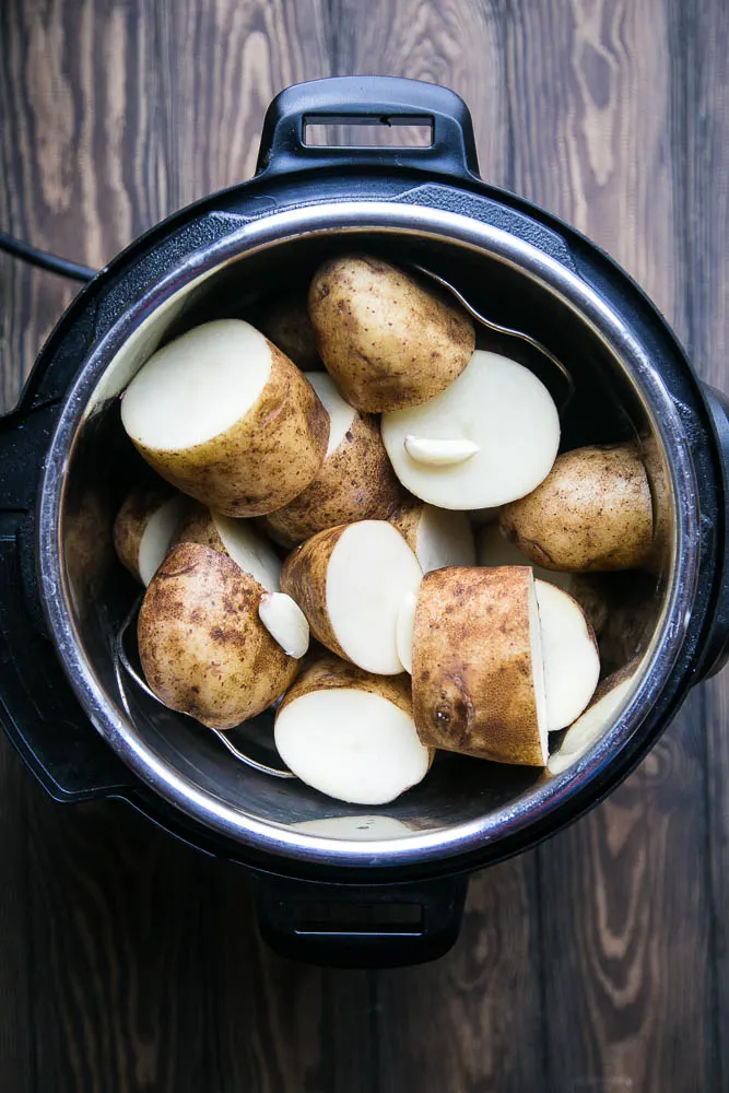 View inside Instant Pot of large chunks of raw potato with garlic cloves.
