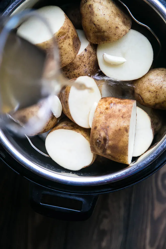 Adding broth to the pot with the potatoes and garlic.