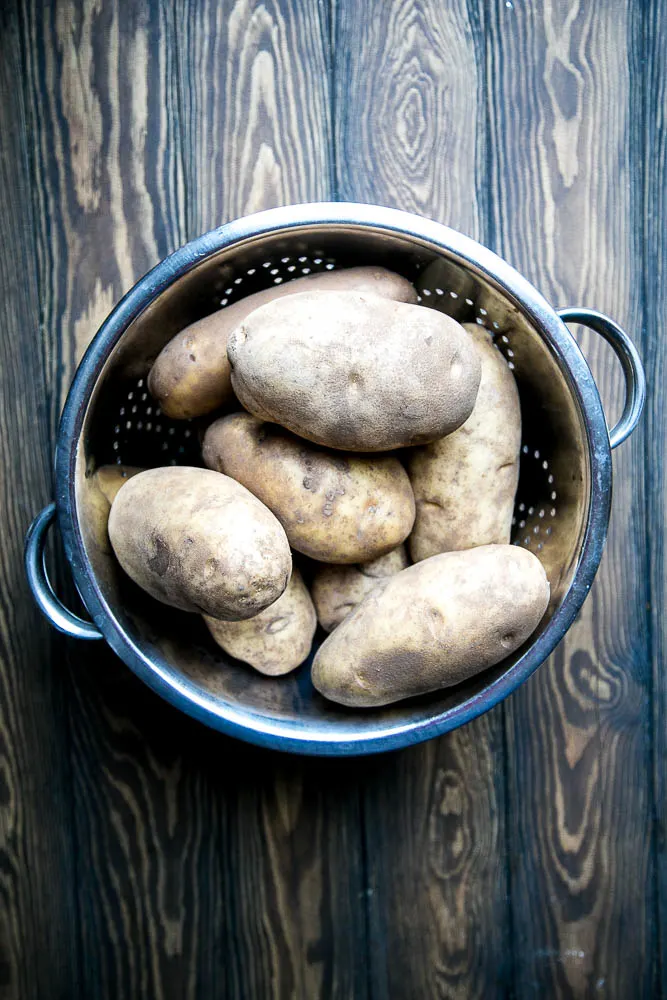 Colander with several whole russet potatoes.