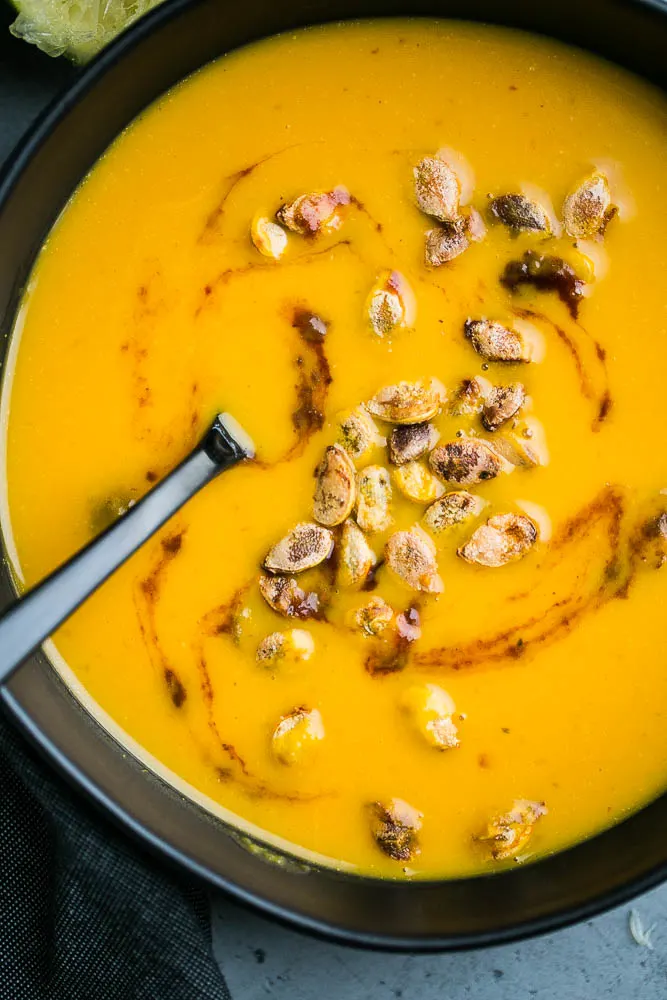 Prep squash ahead of time to make delicious soup! This one is an Indian-inspired butternut squash soup. | perrysplate.com Easy Chipotle Lime Squash Soup in a black bowl with spoon.