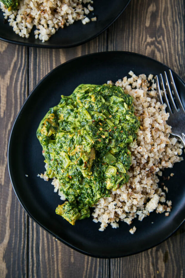 Chicken Saag over roasted cauliflower rice on a black plate.