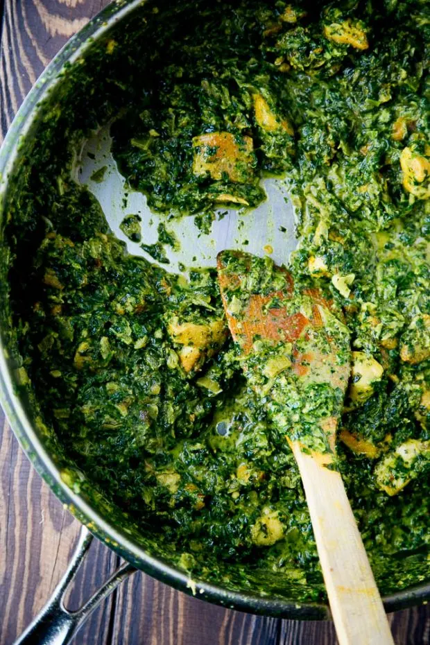 Finished Chicken Saag shown in a deep skillet with a wooden serving spoon.