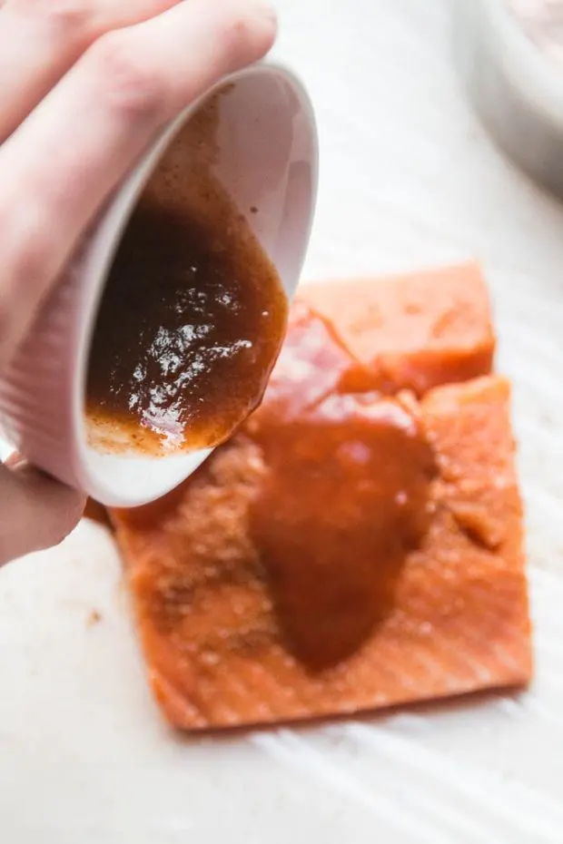 Pouring sriracha and lime over the salmon fillet to prepare it for curing.