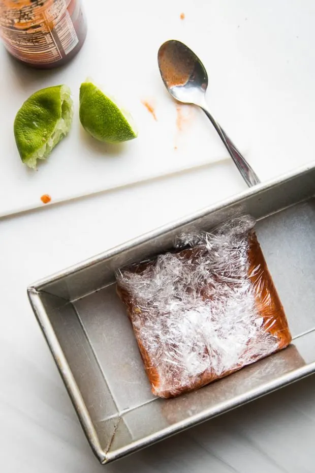 Dressed salmon is wrapped in plastic wrap and placed in a bread pan.