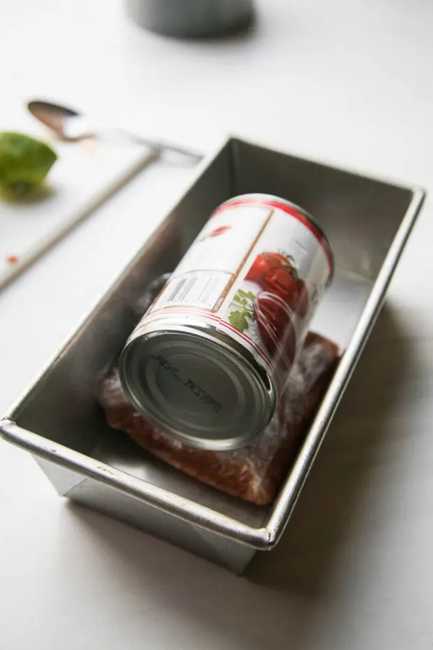 A can of tomatoes sits on the wrapped piece of salmon, compressing it. A can of tomatoes sits on the wrapped piece of salmon, compressing it.