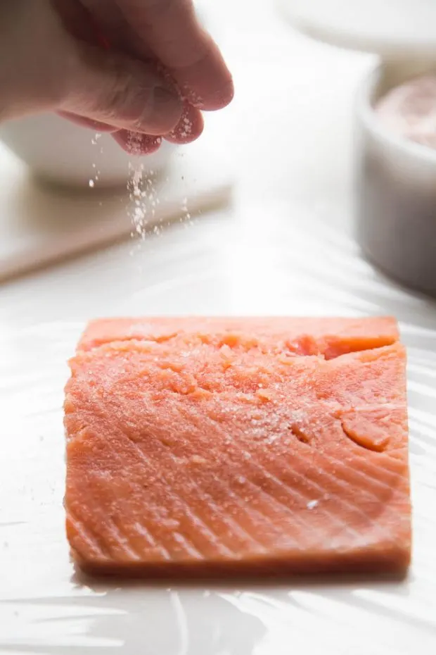 Sprinkling salt on a salmon fillet, getting ready to make homemade gravlax or cured salmon.