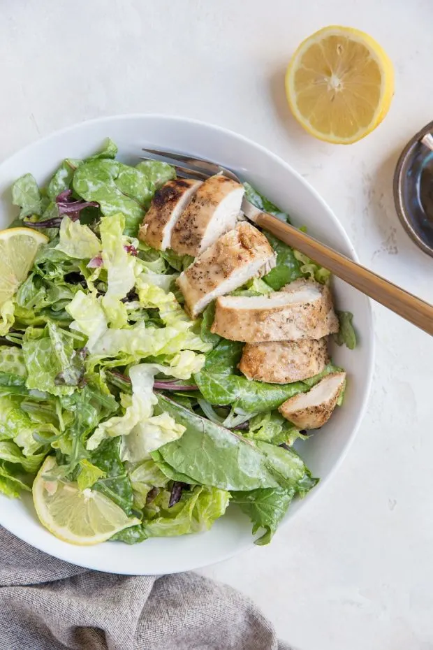 A bowl of caesar salad with baked & sliced balsamic chicken.