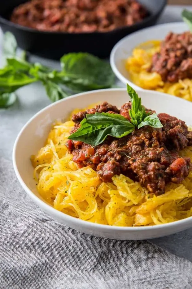 White bowls of spaghetti squash covered in a hearty bolognese sauce and topped with fresh basil.