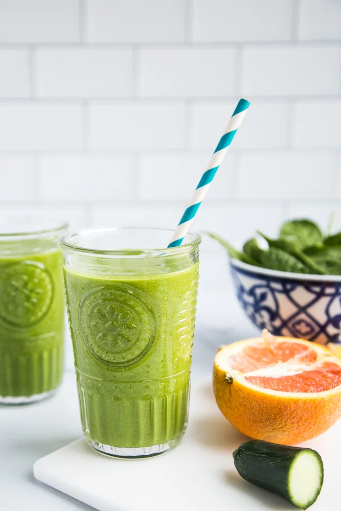 Tasty Green Smoothie Recipe (that actually tastes good!) perrysplate.com Two clear glasses filled with the bright green smoothie. One has a blue striped straw.