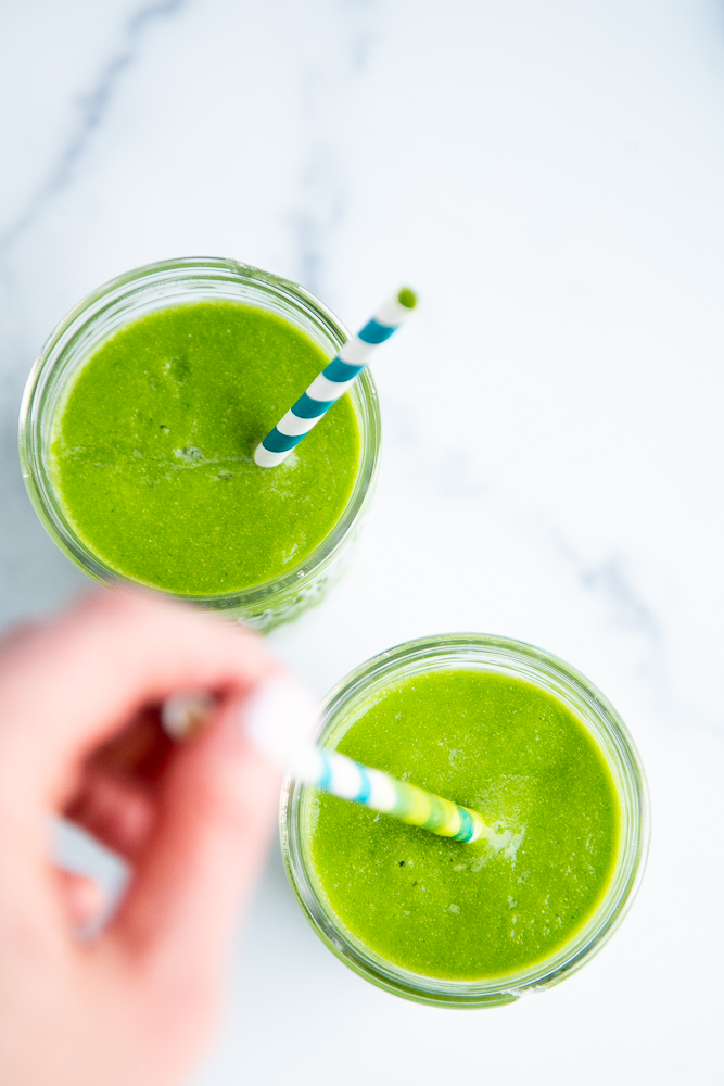 A bright green smoothie with a blue striped straw -- top down view.