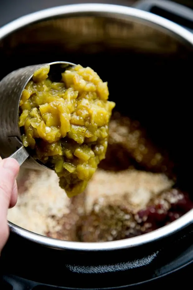 Adding a cup full of diced green chiles to the Instant Pot insert with the beef roast.