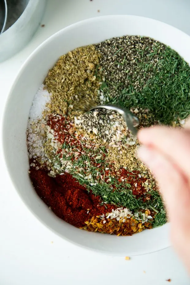 Homemade Montreal style steak seasoning being mixed together in a white bowl with a spoon.