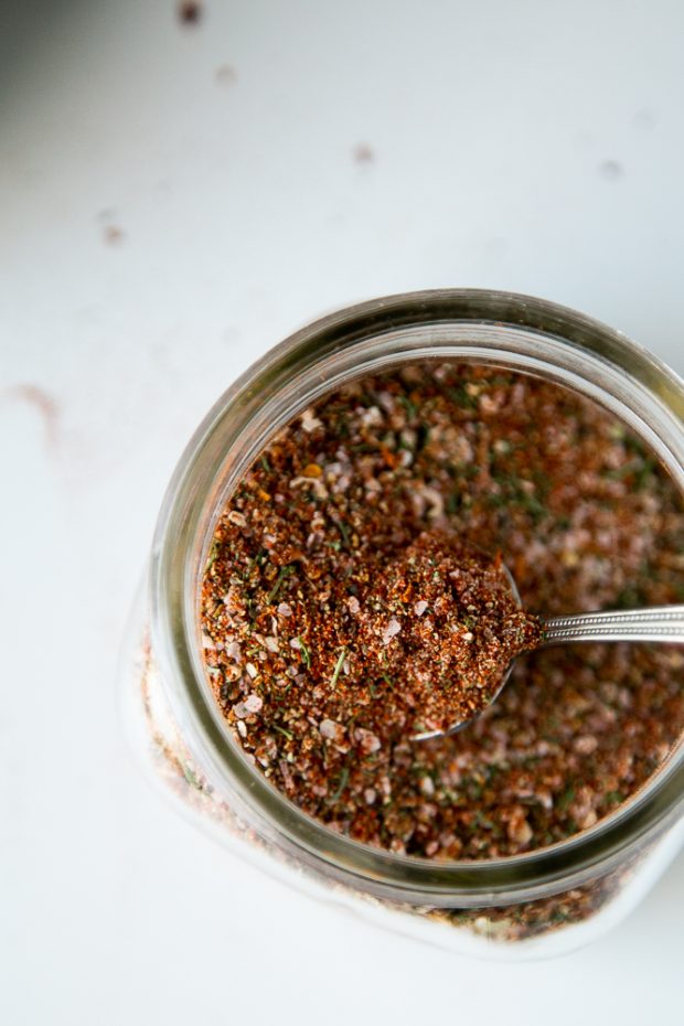 Homemade Montreal Steak Seasoning in a glass jar with a spoon inside.