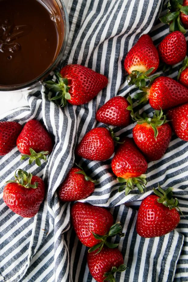 Washed strawberries on a black and white striped towel sitting next to a bowl of melted chocolate.