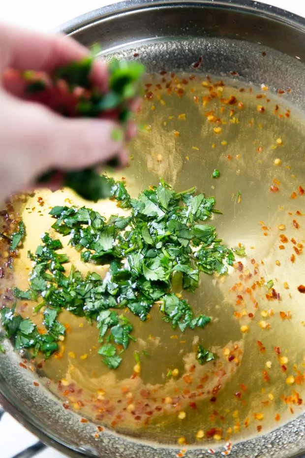 Fresh, chopped cilantro being sprinkled into a stainless skillet with Hot Honey Cilantro Glaze.
