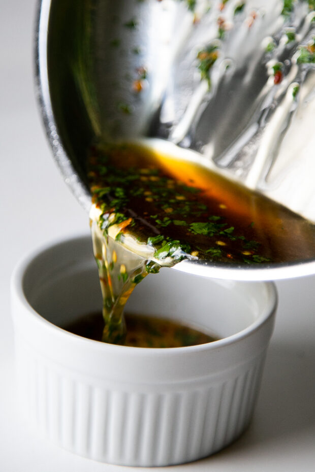Hot Honey Cilantro Glaze being poured from a stainless skillet into a white ramekin. We love this glaze on all kinds of dishes!