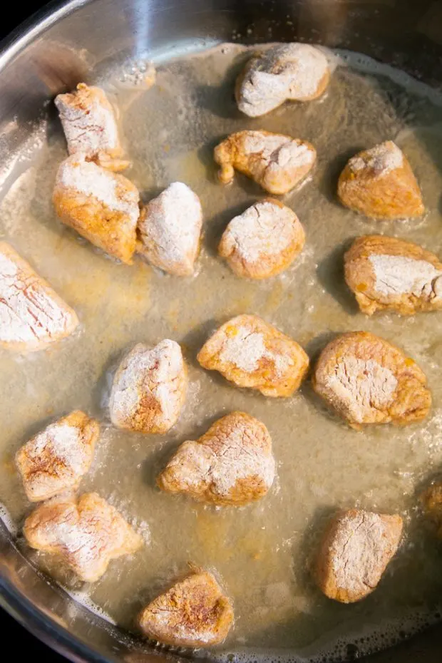 A stainless skillet with hot coconut oil, cooking the chicken pieces.