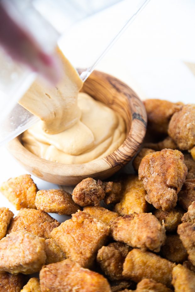 Finished chicken nuggets alongside a bowl of vegan chipotle queso sauce.