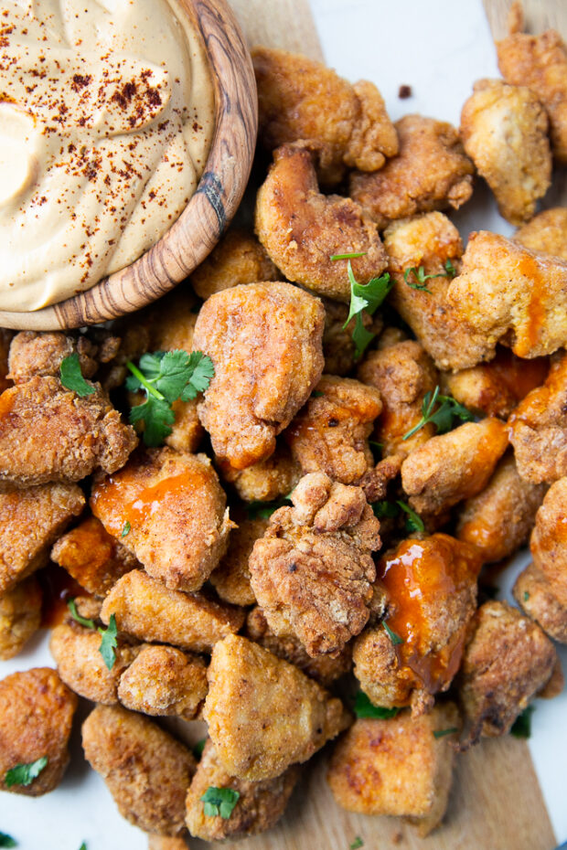 Finished gluten free nuggets alongside the vegan queso sauce. Nuggets have been sprinkled with fresh cilantro and a little hot sauce.