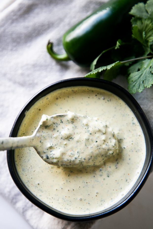 Roasted Jalapeno Ranch Dressing in a black bowl next to some cilantro and a fresh jalapeno pepper.