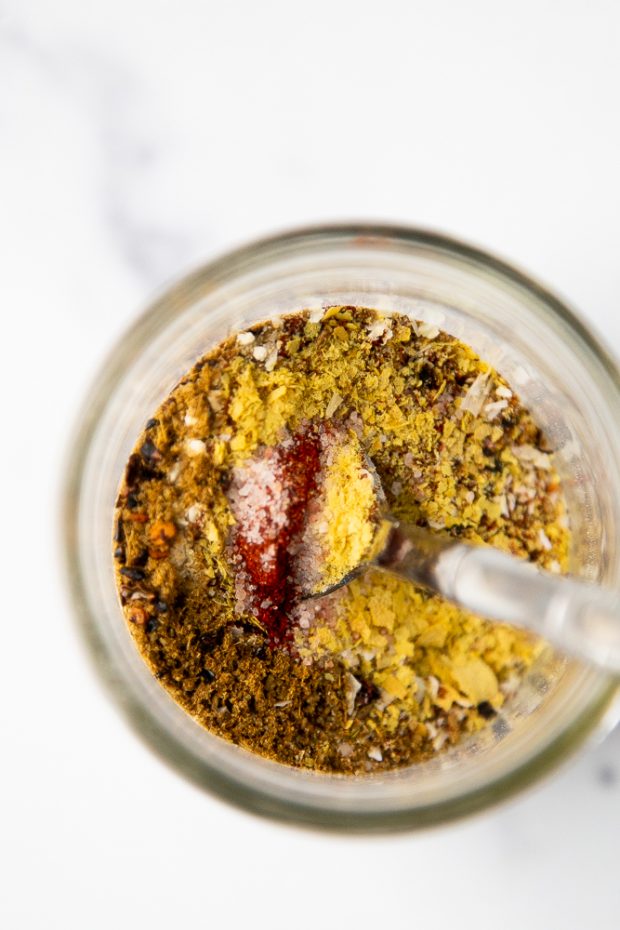 Homemade Smoky Chipotle Taco Seasoning being mixed in a glass jar with a spoon. 