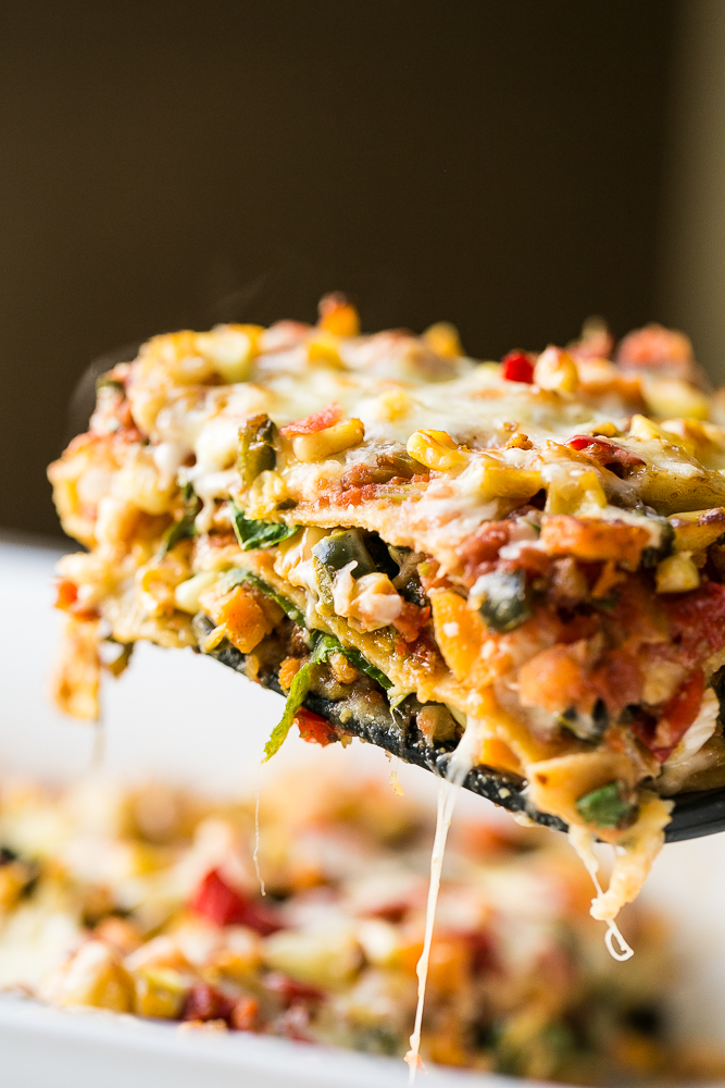 A cheesy slice of Stacked Roasted Vegetable Enchiladas lifted out of a serving dish.