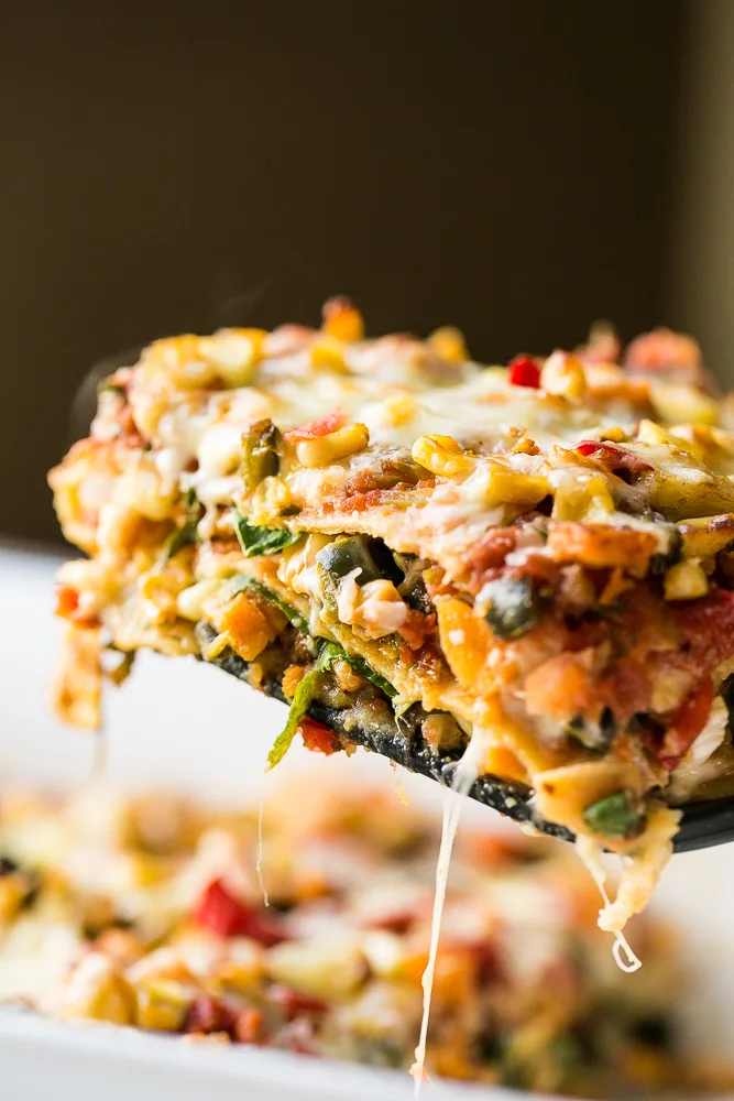 Stacked Roasted Vegetable Enchiladas A cheesy slice of Stacked Roasted Vegetable Enchiladas lifted out of a serving dish.