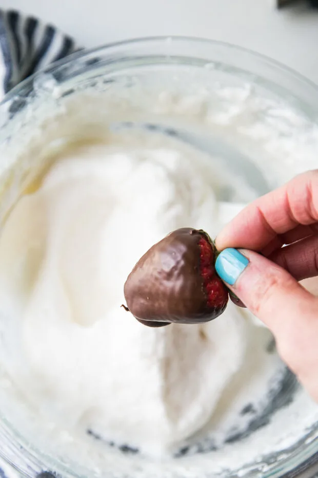A chilled chocolate covered strawberry being dipped in marshmallow fluff.