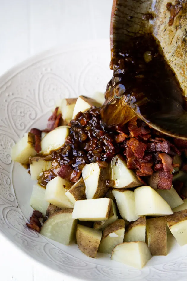 Pouring warm bacon dressing over cooked potatoes to make German Potato Salad.