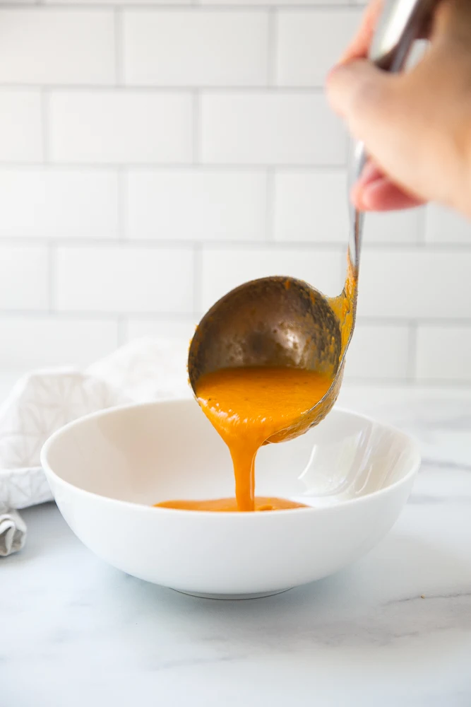 Creamy, roasted tomato soup ladled into a white bowl for serving.