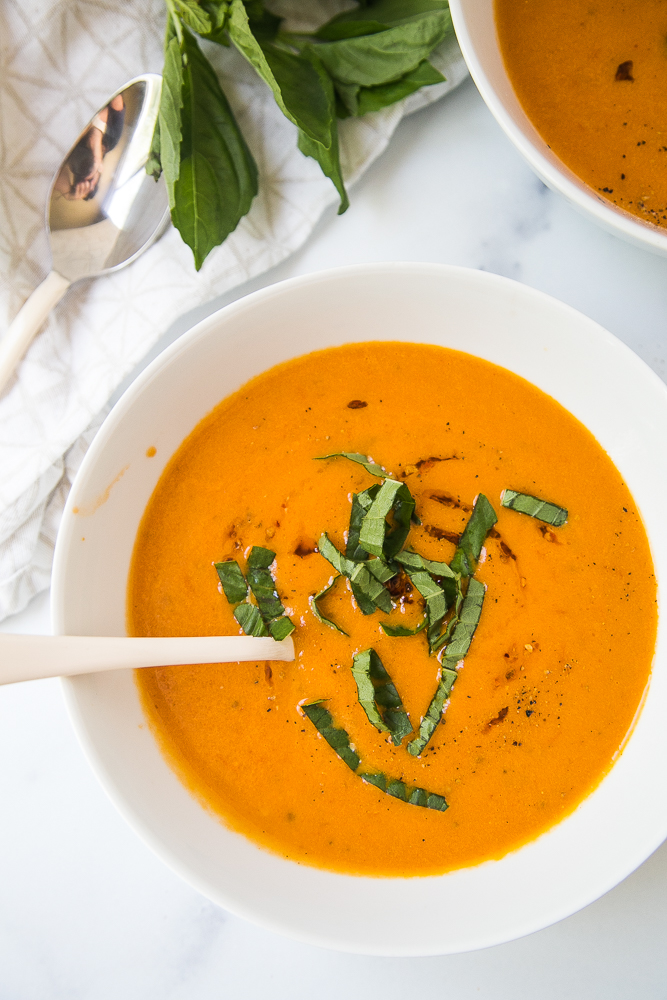 A lovely bowl of simple tomato soup garnished with basil, pepper, and chili oil.