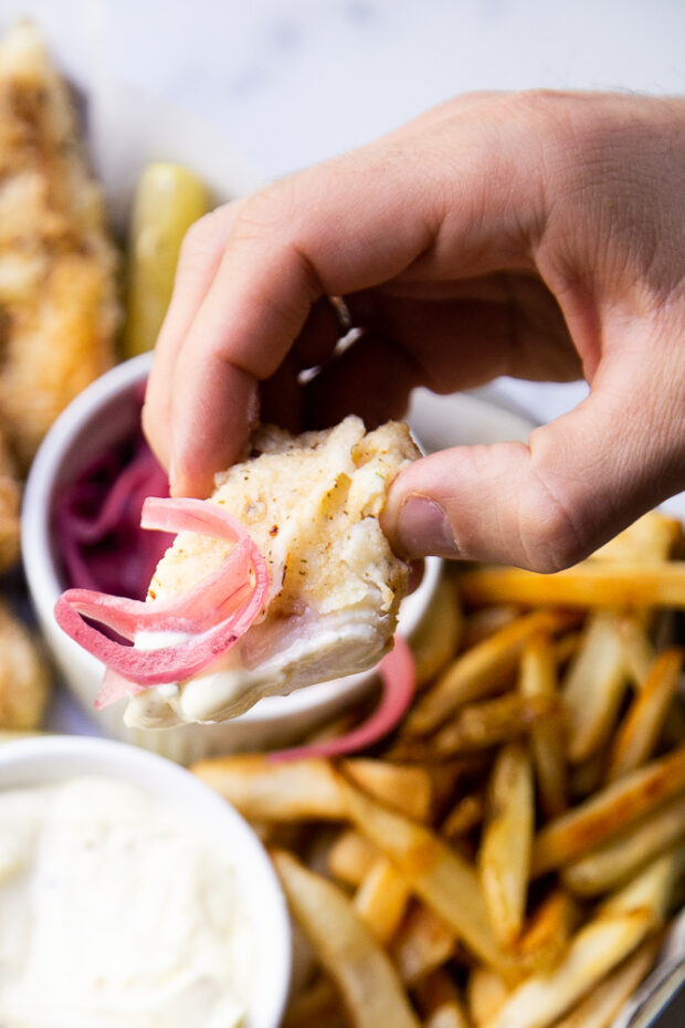 A piece of fried cod dipped in garlic aioli and topped with pickled red onions.