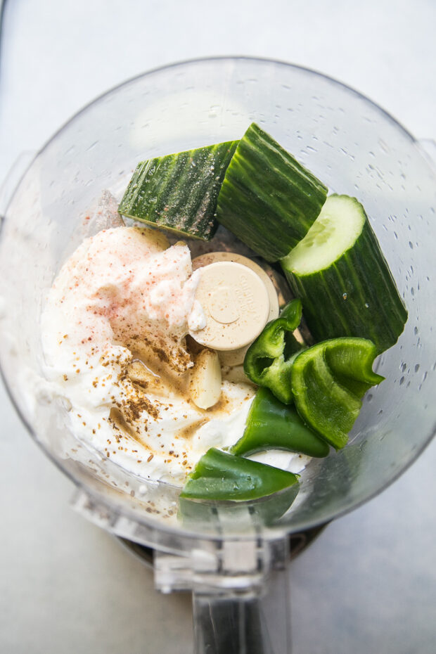 Ingredients for Cucumber Yogurt Dressing in a food processor -- Greek Yogurt, English cucumber, jalapeno, salt, cumin, lemon juice.