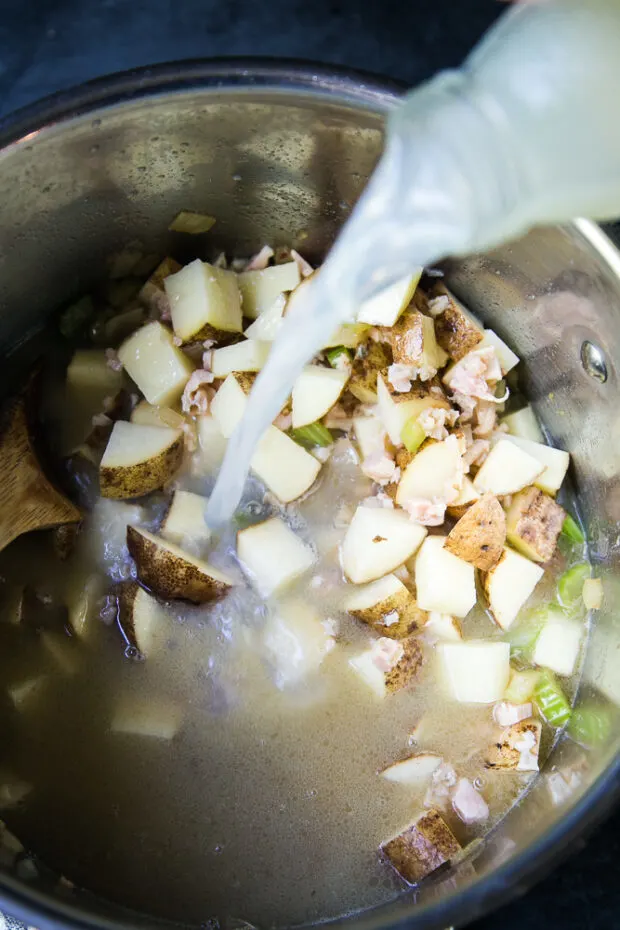 Adding clam juice to the pot with the vegetables and clams.