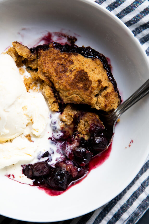 Warm Gluten-Free Berry Cobbler in a bowl with vanilla ice cream.