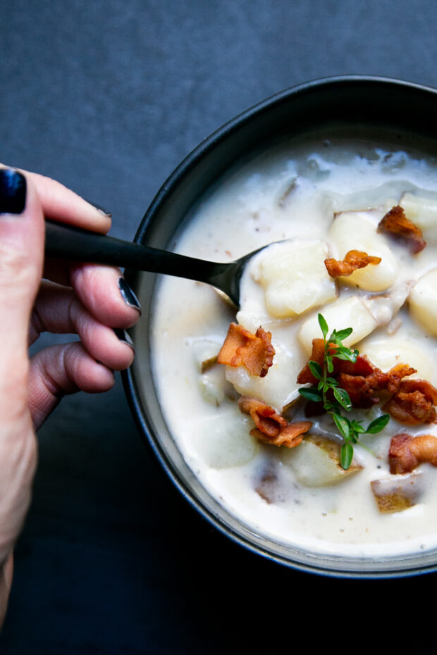 Gluten-Free Clam Chowder with bacon & fresh thyme as a garnish is ladled into a black bowl.