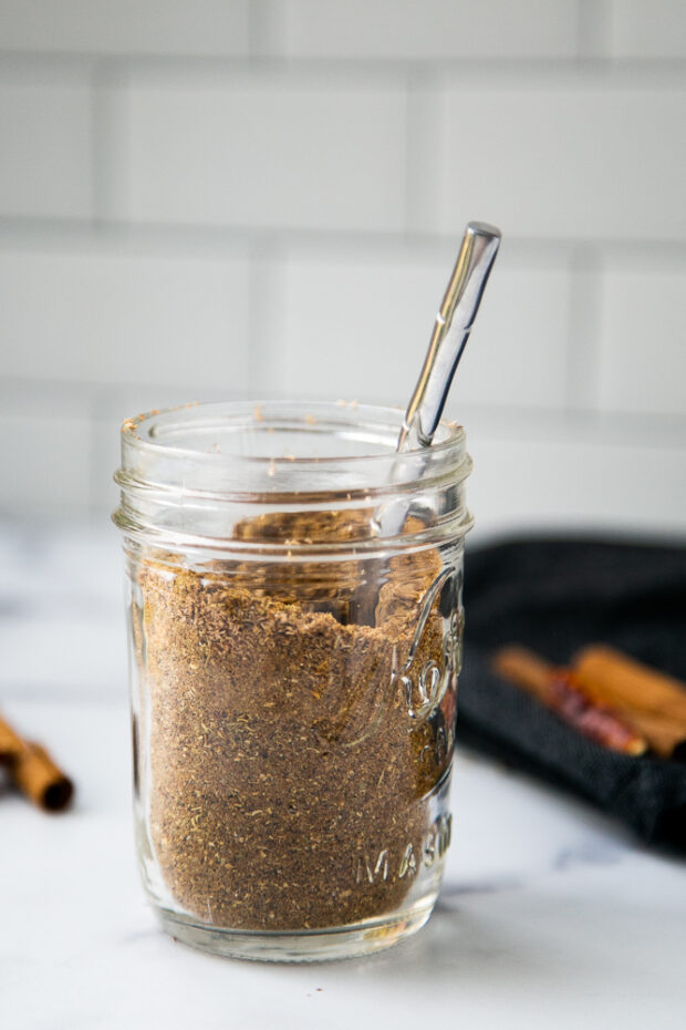 Garam Masala spice blend in a small glass mason jar with a silver spoon inserted. Ready to use!