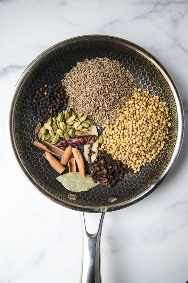 An arrangement of whole spices in a skillet ready for toasting. The spices will be ground to make garam masala.