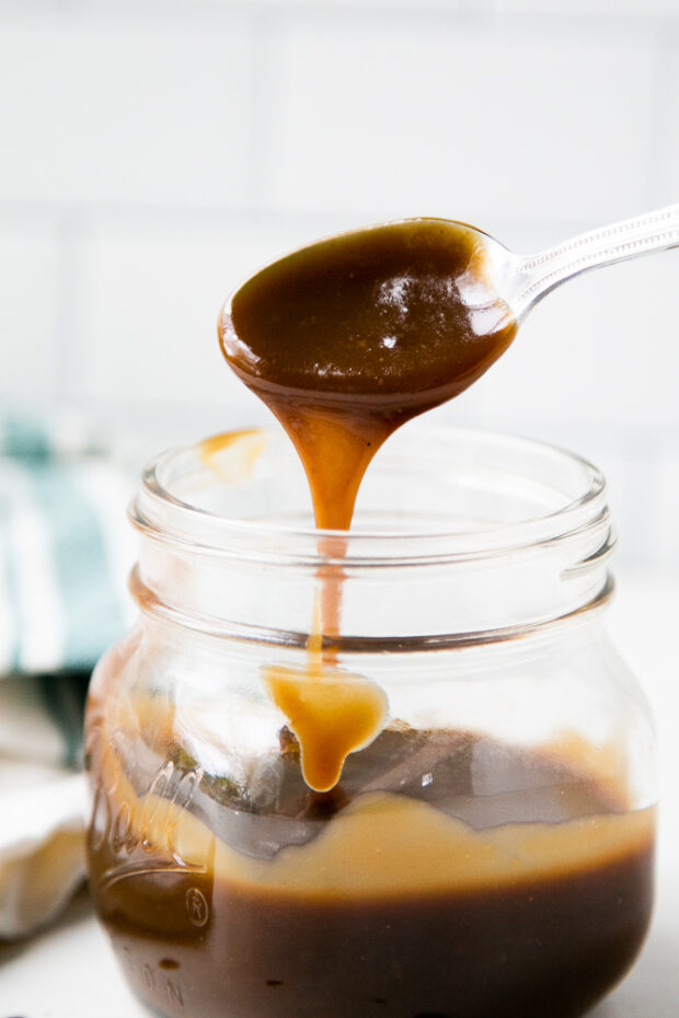 Salted caramel sauce dripping off of a spoon back into the jar.