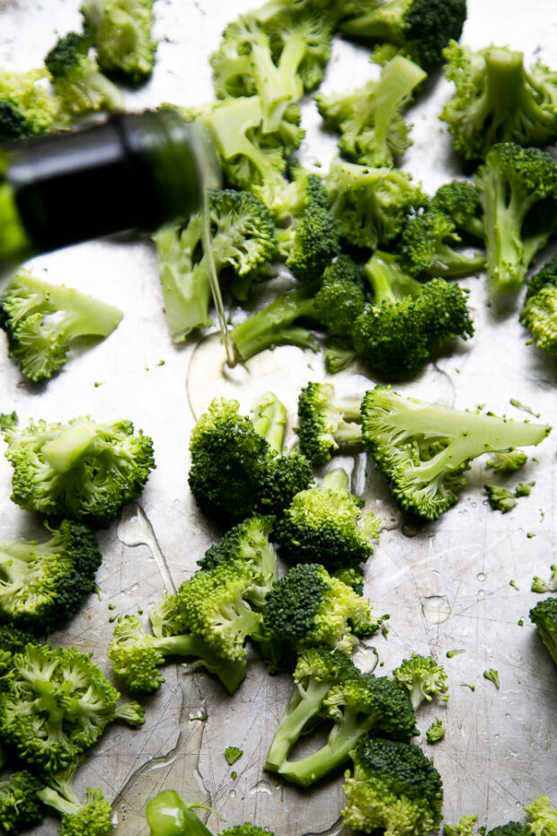 Raw broccoli on a sheet pan drizzled with avocado oil.