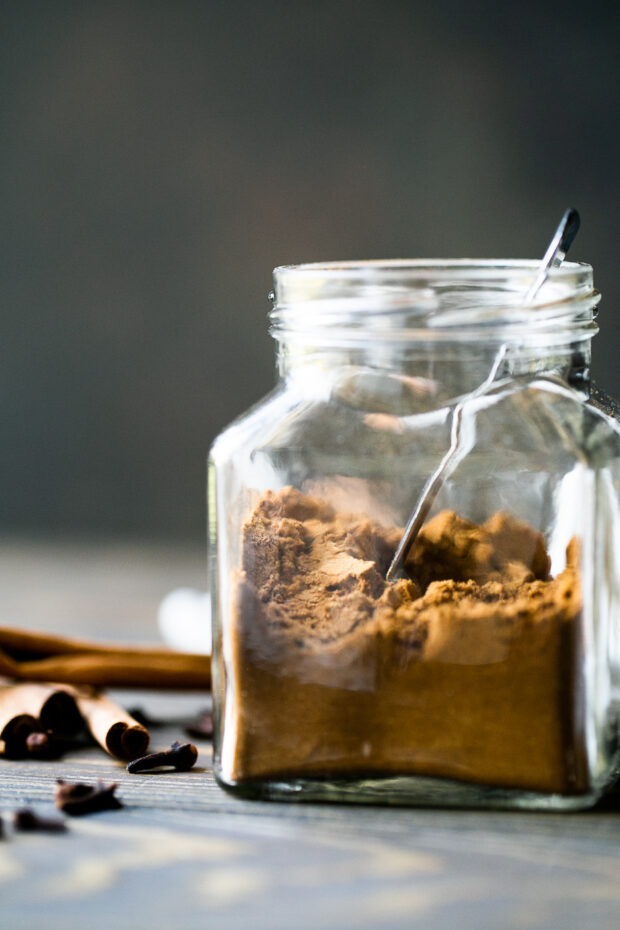 A small jar of pumpkin pie spice -- view from the side. Jar contains a measuring spoon.