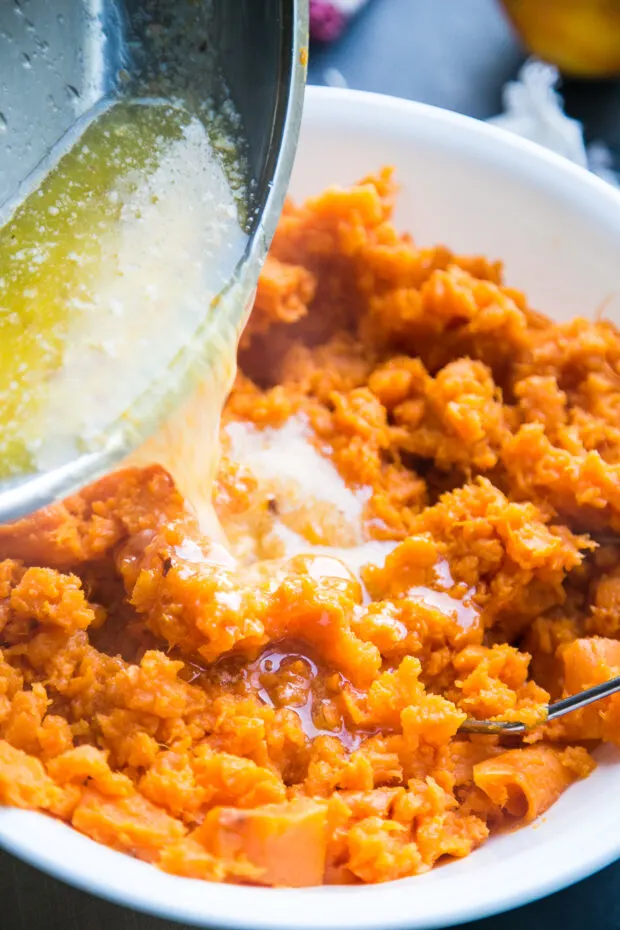 Orange-chili butter is being poured into a bowl of mashed sweet potatoes.