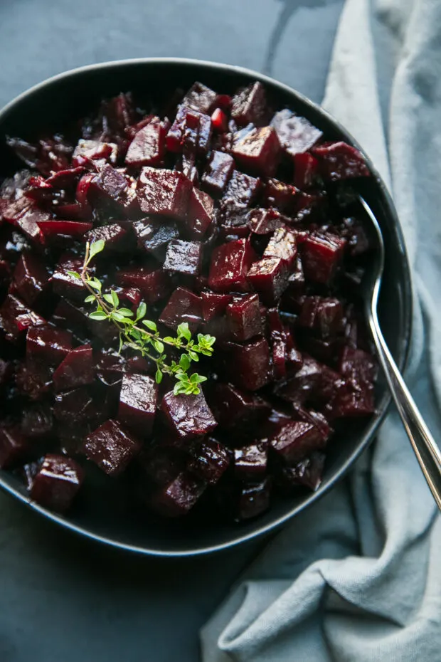 Another shot of this beet recipe -- Sauteed Beets with Balsamic-Orange Glaze in a black bowl topped with a sprig of fresh thyme.