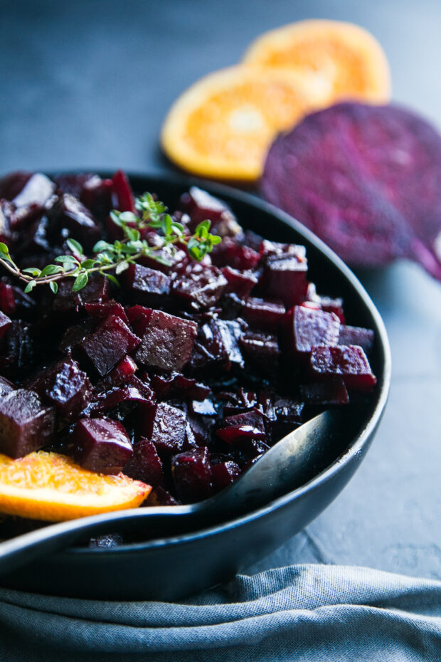 A great beet recipe! This photo shows the sauteed beets in a black bowl topped with a sprig of thyme. You can see sliced beets and oranges in the background.